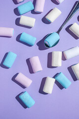 Multicolored marshmallows and a spoon on a purple background.