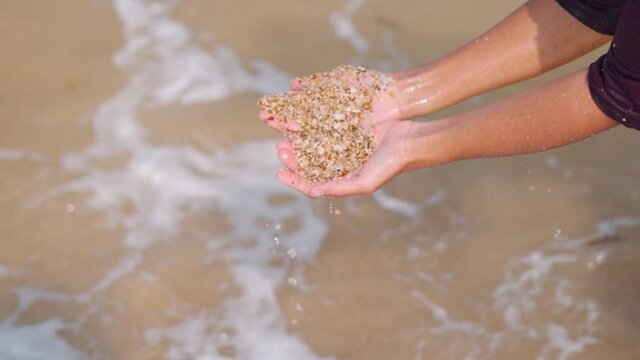 Close up shot of Indian woman with cupped hands holding ocean sand at beach. Female playing at beach with sand in India. concept for sea, summer, vacation, travel