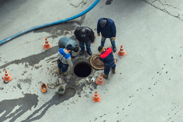 Workers stand over an open manhole on the street. Repair of sewerage, underground utilities