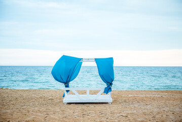 gazebo on the beach at sunset with folding blue curtains, no people 