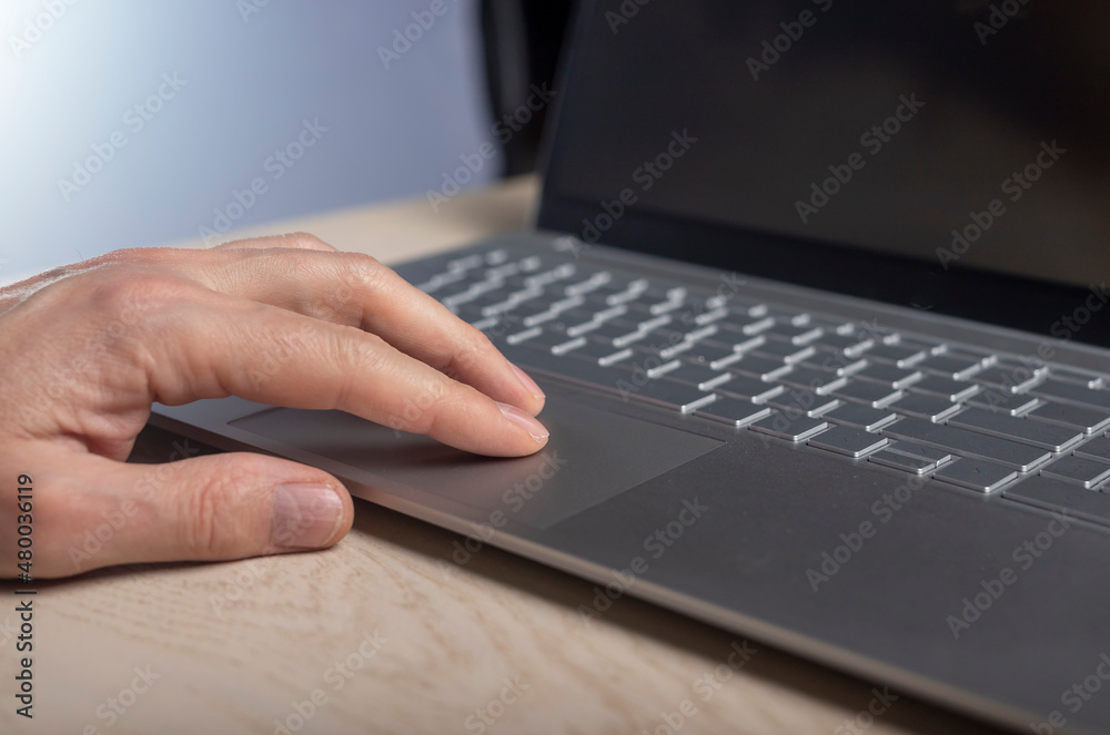 Poster hand on laptop touchpad, tapping and scrolling with fingers close up.