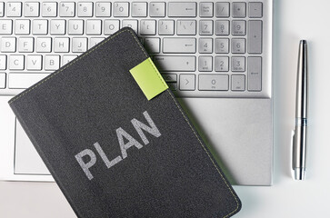 Plan word on business planner notebook on laptop keyboard and pen of silver color, top view.