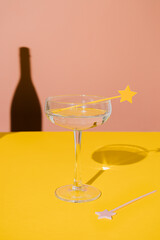 Champagne coupe glass with a star cake pick topper and a sharp champagne shadow on yellow and pink vivid background. Minimal modern still life. Party celebration concept. Luxury concept.