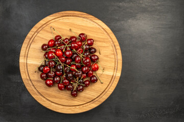 Fresh ripe sour cherries on wooden plate on gray background. Red juicy cherries. Sweet cherry background.