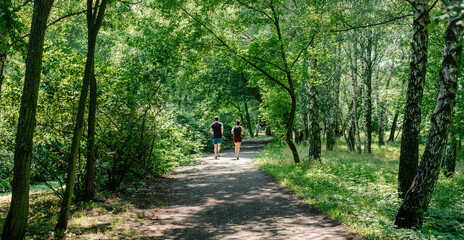 Fototapeta premium A young woman and a young man are running in the distance on a trail in a public park. 