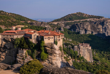 Fototapeta na wymiar Beautiful scenic view of Orthodox Monastery of Áyios Nikólaos Anapafsás (St. Nicholas Anapafsas) on cliff, at the background of stone wall and rock formations of Meteora mountain, Greece.