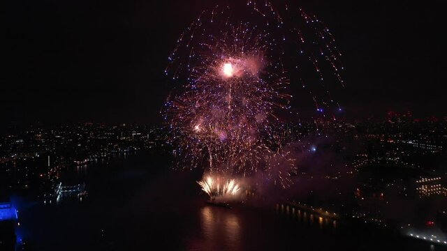 Aerial drone spectacular night video of firework show with dazzling colours glowing over river Thames to celebrate new year's eve, London, United Kingdom