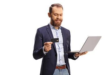 Bearded young man looking at a credit card and holding a laptop computer