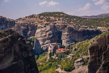 Fototapeta na wymiar Beautiful scenic view of Orthodox Monastery of Rousanoú (St.Barbara) on cliff, immense monolithic pillar, at the background of stone wall and rock formations of Meteora mountain, Greece.