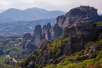 Fototapeta na wymiar Beautiful scenic view of Orthodox Monastery of Rousanoú (St.Barbara) on cliff, immense monolithic pillar, at the background of stone wall and rock formations of Meteora mountain, Greece.