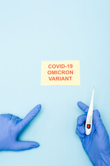 partial view of doctor with electronic thermometer pointing at card with covid-19 omicron variant...