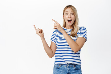 Advertisement. Portrant of stylish modern girl with blond hair, pointing fingers left at copy space, showing logo or banner, company name on empty place, white background
