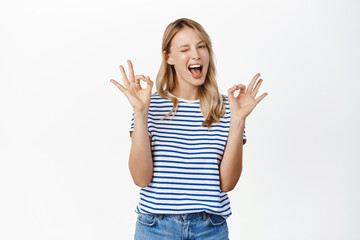 Perfect, very good. Smiling attractive young woman showing okay, ok gesture and looking satisfied, recommending great product, praise or approve smth, white background