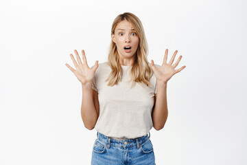 Shocked blond girl raising hands up and screaming amazed, looking in awe at camear, being scared or startled, standing over white background