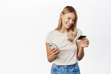 Young smiling woman paying with mobile phone, shop online on smartphone application, holding credit card, white background