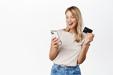Happy smiling woman with mobile phone, showing credit card and laughing, demonstrating paying app, bank offer for contactless online shopping pay, white background