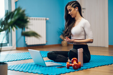 Attractive fitness instructor coaching an online class while using a laptop