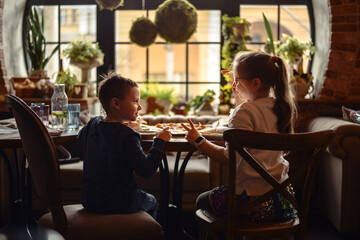 Friends, children, a boy and a girl are sitting in a cafe, eating pizza and talking, smiling.