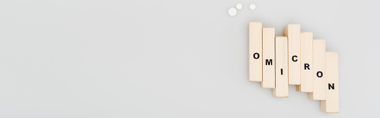 top view of wooden bricks with omicron lettering near pills on grey background, banner.