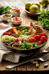 Healthy meal with assorted vegetables, millet and grilled chicken breasts in a ceramic bowl on a wooden rustic table, close up view