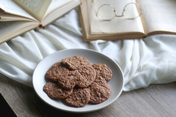 Plate of healthy gluten free cookies, open books and reading glasses on the table. Selective focus.