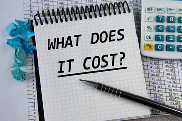 WHAT DOES IT COST? - words in a white notepad on the background of a calculator and a pen
