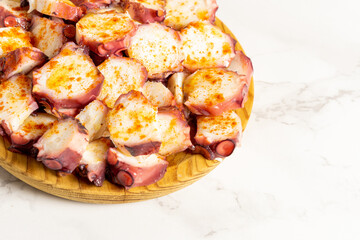 A closeup photo of pulpo a la gallega, an octopus with boiled potatoes, typical Spanish Galician dish, on a traditional wooden plate, with copy space. High quality photo