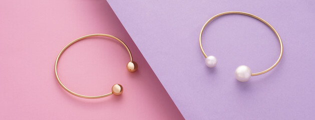 Panoramic shot of Two modern golden with pearls bracelets on pink and purple slanted background