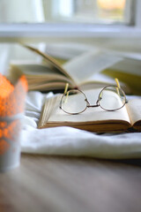 Open books, reading glasses and lit candle on the table. Selective focus.