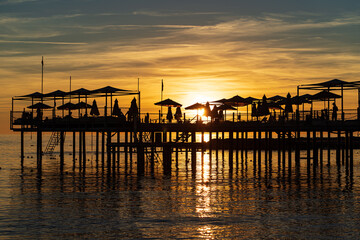 Fototapeta premium pier with umbrellas and sunbeds. silhouettes. beautiful sunset on sea. 