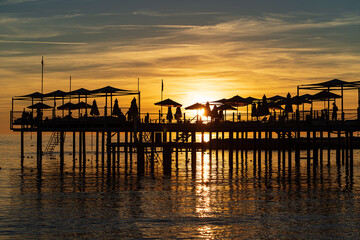 Fototapeta na wymiar pier with umbrellas and sunbeds. silhouettes. beautiful sunset on sea. 