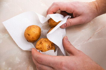 A man dries raw, washed potatoes with paper towels and napkins to bake them in foil in the oven.