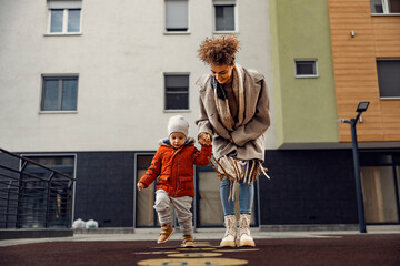 A babysitter teaching a child how to play hopscotch at the playground. - obrazy, fototapety, plakaty