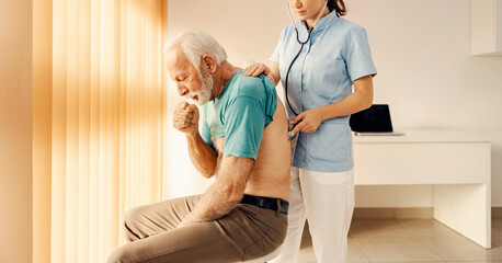 A sick old man coughing and getting medical attention by a female doctor in doctor's office. Heath care, medical support and medical service. - obrazy, fototapety, plakaty