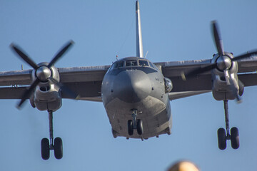 A military transport aircraft comes in for landing with landing gear extended against a clear sky