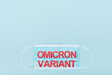 top view of medical mask with red omicron variant lettering on blue background with copy space.