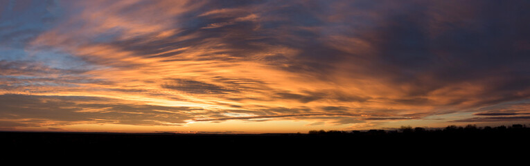 Fototapeta premium Sunset panorama with dark yellow clouds over a small town against the blue sky