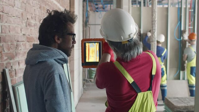 Rear view of owner and foreman examine construction site with infrared camera. Realtime