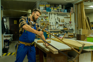 Handsome young carpenter cutting the board using the old carpenter saw