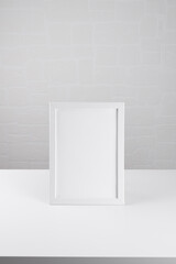 Portrait a4 white wooden frame mockup on the white table on white wall background, poster mockup. Clean, modern, minimal frame. Empty frame Indoor interior, show text or product