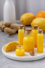 Ginger shots in a small glass bottles. Immune boosting ginger drink with ingredients ginger root, lemon, orange on background. Close up, vertical, selective focus, gray concrete background.