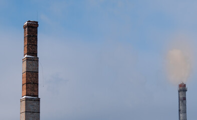 Old brick chimney on blurred background of smoky sky and modern steaming pipe