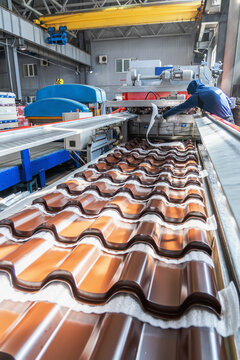 Roof metal tile production line on automatic forming machine in factory, metalwork industry.