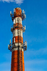 Factory chimney (brick tube) with mobile antennas against blue sky