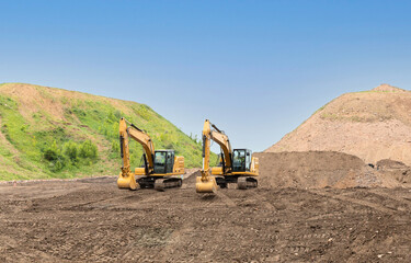 Two yellow excavators move soil on the road construction site