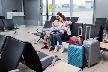 girl sleeping on knees of tired parents in airport lounge.