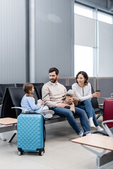 happy parents looking at daughter with smartphone in airport.