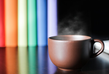 Brown cup with hot latte on purple work desk, headphones and books with lgbt movement colors