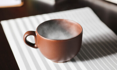 brown cup of coffee, with hot steam, on the work desk