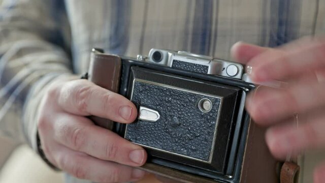 Close-up vintage photo camera details, setting up the film camera. Hands of middle aged man use manual aperture ring on the manual lens.